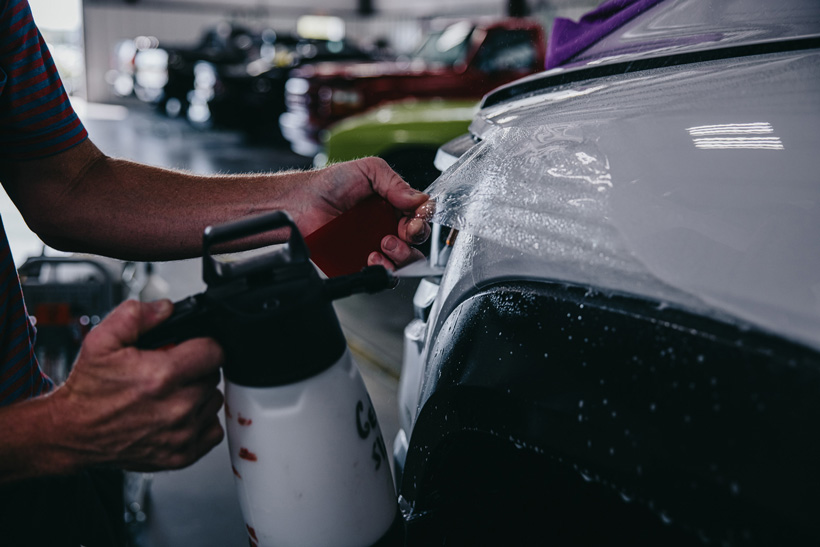 A close up photo of someone adhering a protective coating to a white vehicle.