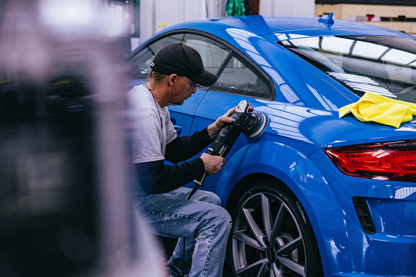 A Detail Depot employee buffs the exterior of a cobalt blue Audi.