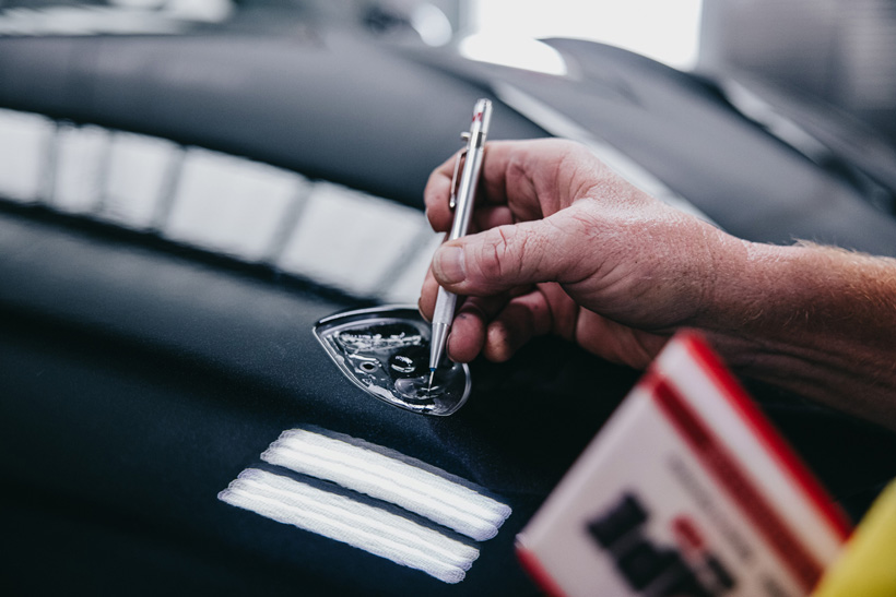 A worker carefully details around the emblem on a black Porsche.
