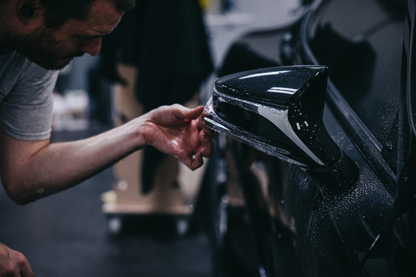A detail depot employee carefully apply paint protection film to a car.