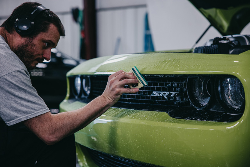 A detail depot employee carefully detailing the front grill of a lime green Dodge Challenger SRT.